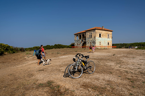 Torre Astura, Italy - September 12, 2021, People and bicycles near a dilapidated house on the beach in Torre Astura, Italy