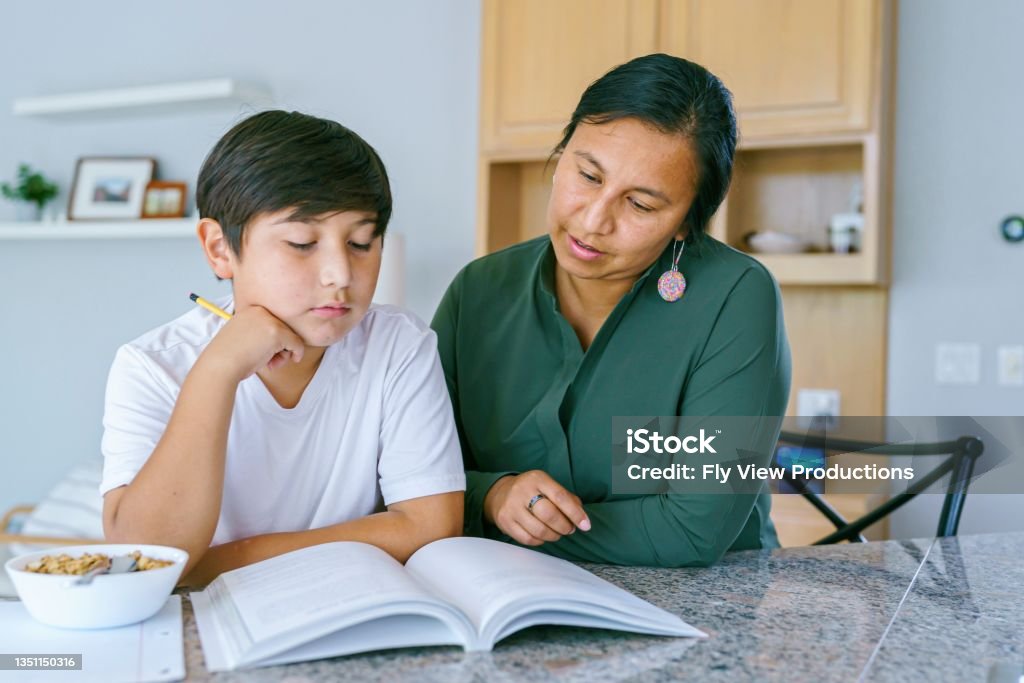 Native American mom helping son with homework A Native American boy in Middle School sits at the kitchen counter and works on homework with his mom's assistance. Indigenous Peoples of the Americas Stock Photo
