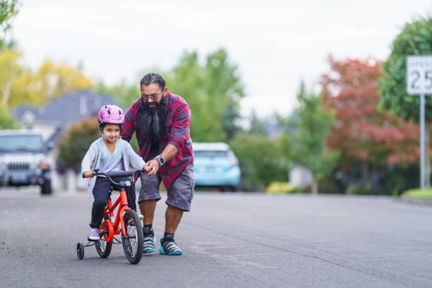 Native American dad helping his young daughter learn to ride a bike stock photo