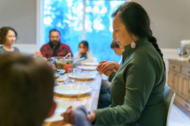 Friends and family holding hands and praying before holiday dinner Multi-ethnic group of adults and children hold hands and give thanks with prayer while sitting around dinner table before holiday meal with friends and extended family. indian dinner stock pictures, royalty-free photos & images