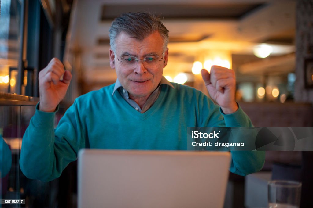 Senior man watching a sport match Mature man with hands up, cheerleading, watching a sport game on his laptop. Men Stock Photo