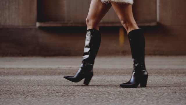 Young Woman In Black Leather Boots Walking Along Street