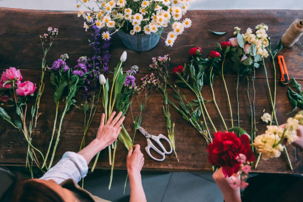 Florist making fashion modern bouquet of different flowers Florist makes a trendy modern bouquet of different flowers on a wooden table background. View from above Make stock pictures, royalty-free photos & images