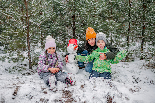 Kids with mom enjoy first snow in winter forest and have fun together, active winter weekend, seasonal outdoor activities, happy family lifestyle