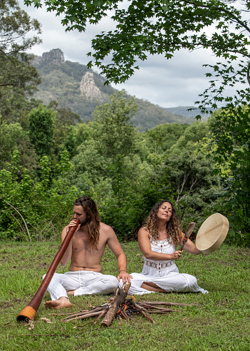 Alternative young couple play didgeridoo and beat drum. The sacred Nimbin rocks are in the background.