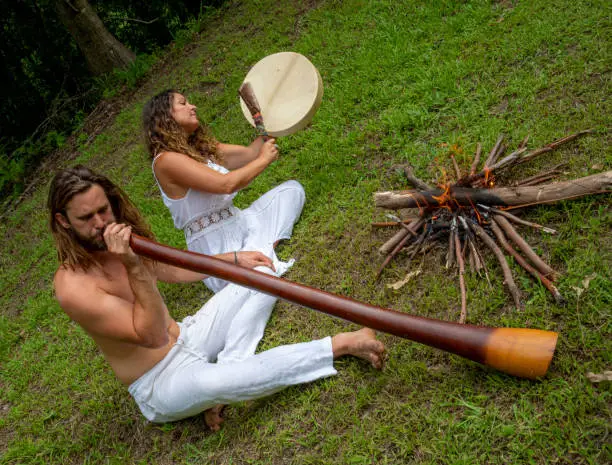 Alternative young couple play didgeridoo and beat drum.