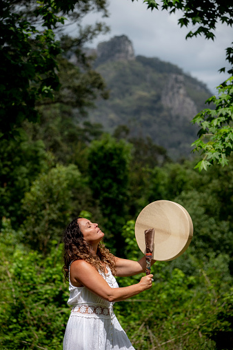 Alternative lifestyle woman beats a drum. It is a form of meditation. The sacred Nimbin Rocks are in the background.