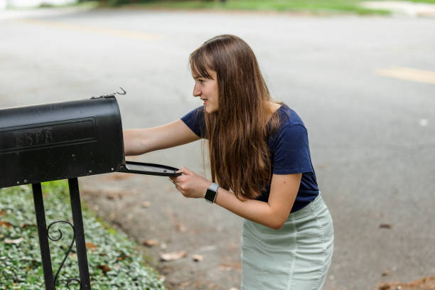 a teen brunette girl with long hair checking the mailbox for letters and packages. - looking into mailbox imagens e fotografias de stock