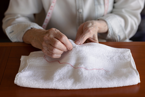 Woaman sewing a red thread on a small white towel.