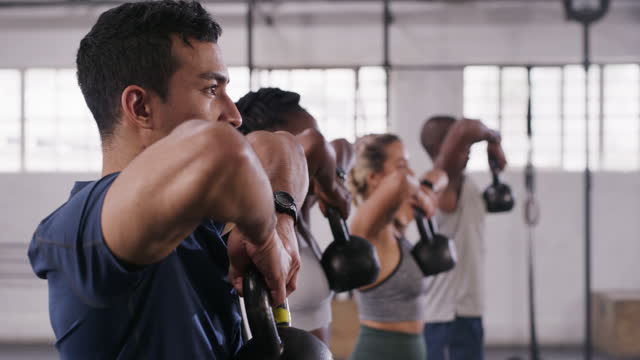4k video footage of a group of young people lifting kettlebells together at the gym