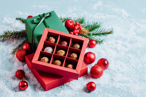 chocolates in a red festive box dark chocolate truffle on a christmas background with new year's toys balls fir branches. flat mock up copy space. - chocolate candy gift package chocolate imagens e fotografias de stock