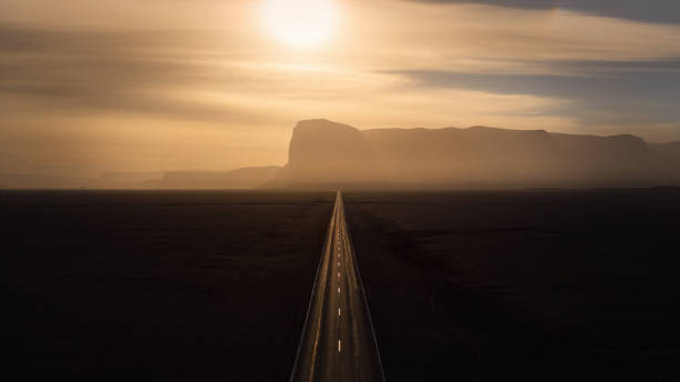Endless Road into the Sunset Endless straight road into the sun between black volcanic gravel towards sunset over icelandic mountain range. Aerial drone point of view along the country highway. Southern Iceland, Golden Circle Route, Iceland, Northern Europe. golden circle route photos stock pictures, royalty-free photos & images