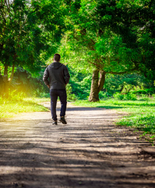 istock Man walking down a desolate road, man walking backwards on a road surrounded by vegetation 1351209672