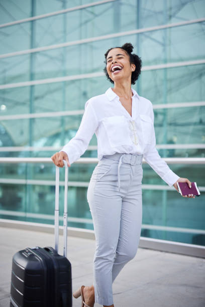 donna d'affari che ride camminando con il passaporto e la valigia fuori da un aeroporto - valigia a rotelle foto e immagini stock