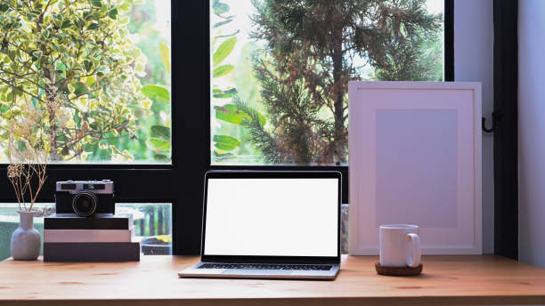 istock Front view laptop computer, picture frame and coffee cup on wooden table near window. 1351210540
