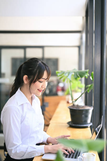 istock Side view smiling young female working with laptop computer in cafe. 1351210631