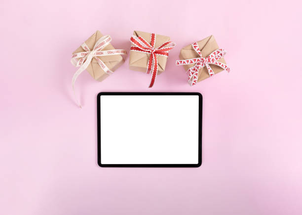 クリスマスプレゼントとピンク色の背景に白い画面とiPadのプロ。フラットレイ。