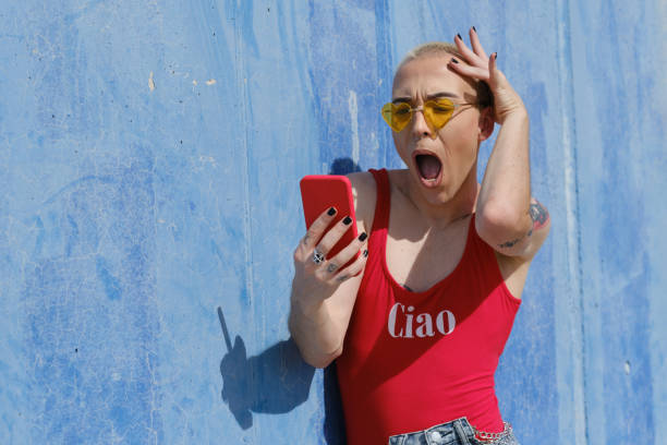 persona no binaria mirando con una expresión de sorpresa y sorpresa en la pantalla del teléfono móvil. - non verbal communication fotografías e imágenes de stock