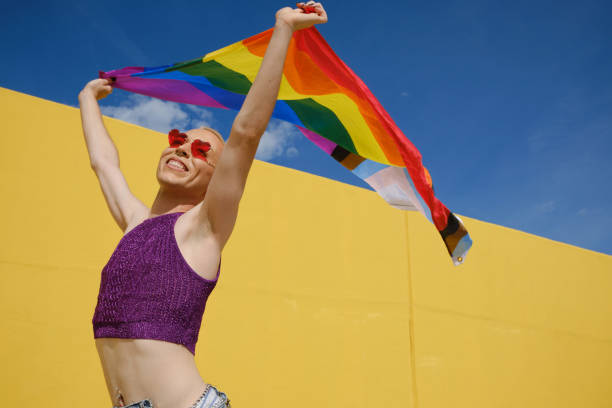 istock Young non-binary person looking happy and excited while waving a rainbow flag outdoors. 1351218918