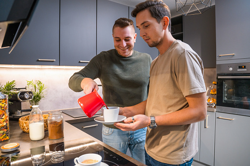 Young adult gay couple preparing coffee. Standing in a kitchen spending quality time talking to each other.