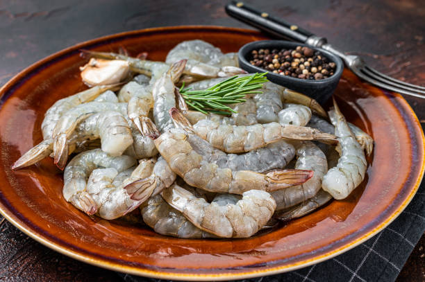 istock Black Raw uncooked Headless giant shrimps prawns in a rustic plate. Dark background. Top view 1351221441