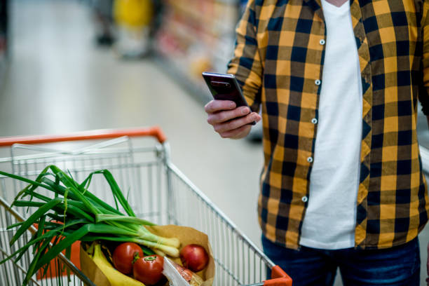 istock Young handsome man in a supermarket using smartphone while grocery shopping 1351222462