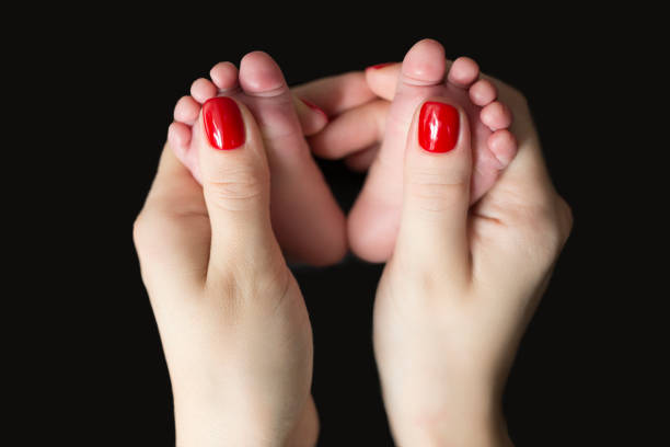 photo of tiny newborn feet hold in mother's hands on the black background. Front wiev.