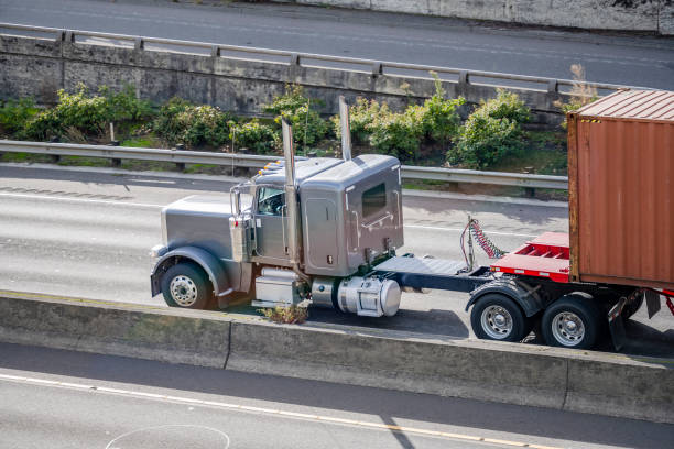 istock Classic gray bonnet American big rig semi truck transporting container on flat bed semi trailer moving fast on the multilevel highway road intersection 1351228670