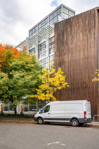 Compact cargo mini van delivered goods to client at multi-apartment high-rise building with wood wall and standing on the autumn street of urban city waiting for unload