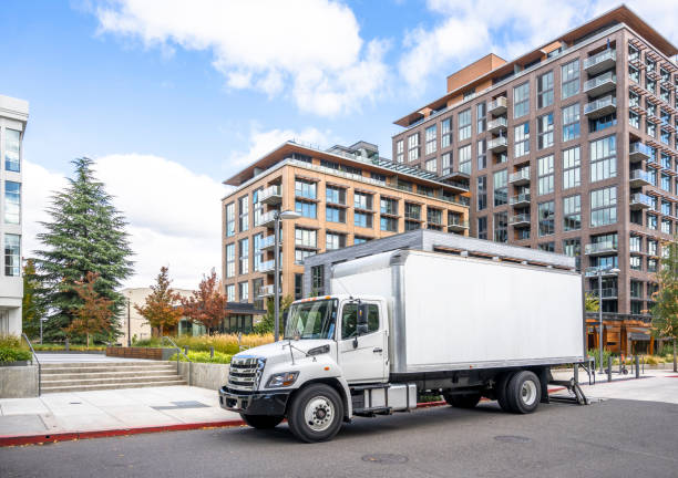 middle size rig white semi truck with box trailer unloading cargo delivered to new multilevel apartment buildings in urban city - the media imagens e fotografias de stock