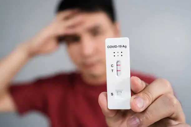 Photo of stressed man holding Coronavirus(Covid-19) positive test result with Antigen Rapid Test kit (ATK)