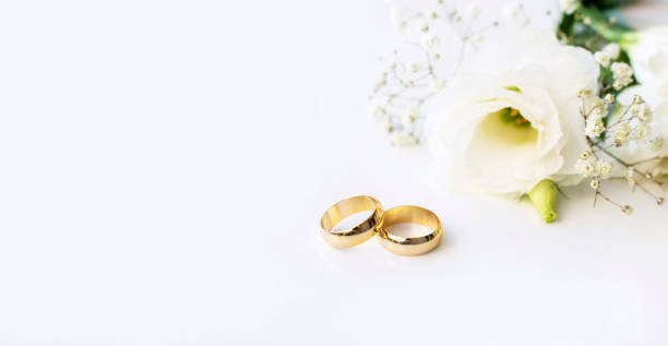 istock White flowers and two golden wedding rings on white background. 1351238211