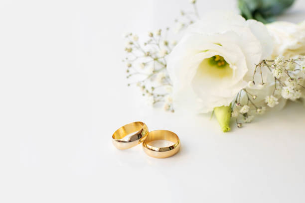 istock White flowers and two golden wedding rings on white background. 1351238281