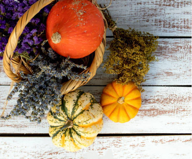 Wooden basket and assorted pumpkins and purple flowers inside on a white aged wooden table.stilllife photo. stock photo