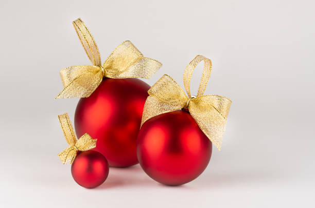 istock Christmas background in simple style - three bright red glossy christmas balls with gold bows stand on soft light white background, closeup, copy space, for design of poster, flyer, card, brochure. 1351247641