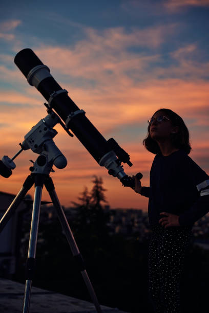 istock Girl with astronomical telescope stargazing under twilight sky. 1351250035