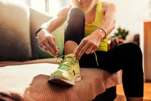 Photo of woman getting ready for a jogging.She ties shoelaces in her living room and gets ready for jogging.Human body part.