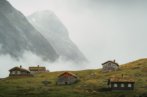 Majestic mountain range covered with fog and huts in the valley