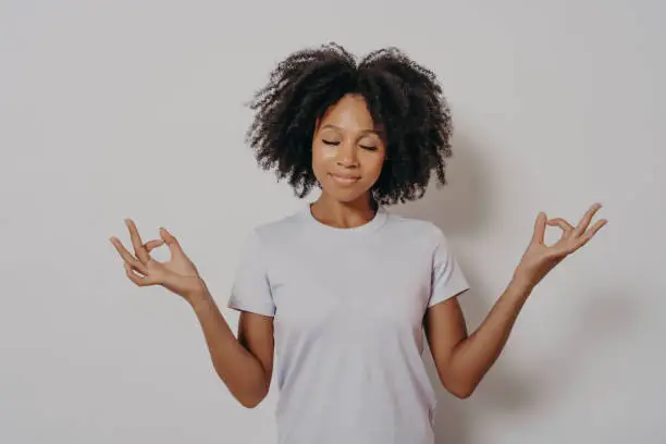 Photo of Calm and peaceful young mixed race woman keeping hands in mudra gesture and eyes closed