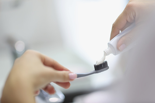 Close-up of person apply toothpaste on toothbrush, preparing to clean teeth in bathroom. Get ready, morning routine, hygiene, body and face care concept. Blurred background