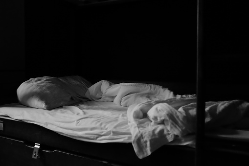 Open messy hostel bed in black and white, moody with copy space