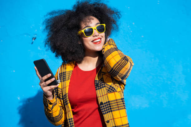 istock Smiling american-african woman using smart phone on a blue background 1351257394