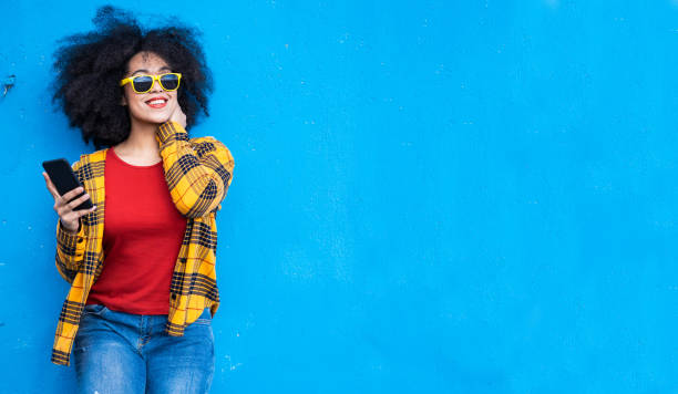 istock Smiling american-african woman using smart phone on a blue background 1351257401