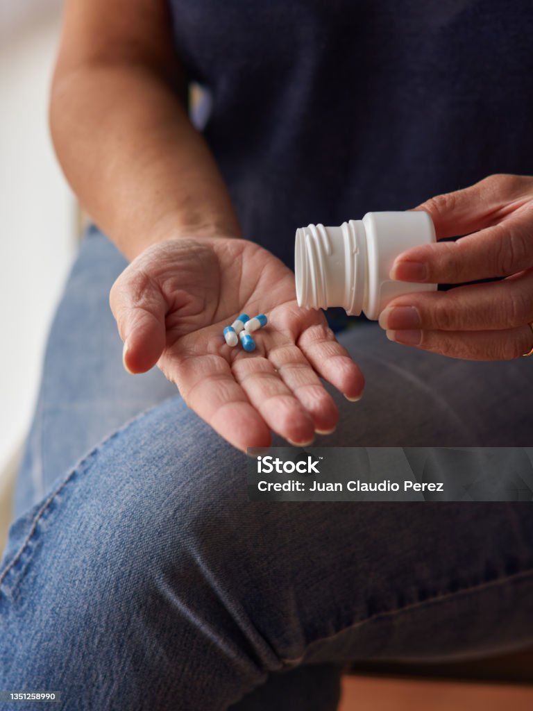 woman sitting at home emptying a box of pills into her hand. Middle-aged Caucasian woman sitting at home emptying a box of pills into her hand. Vertical frame. Taking Medicine Stock Photo