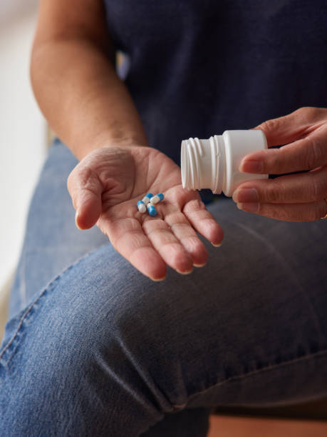 woman sitting at home emptying a box of pills into her hand. Middle-aged Caucasian woman sitting at home emptying a box of pills into her hand. Vertical frame. poison arrow frog photos stock pictures, royalty-free photos & images