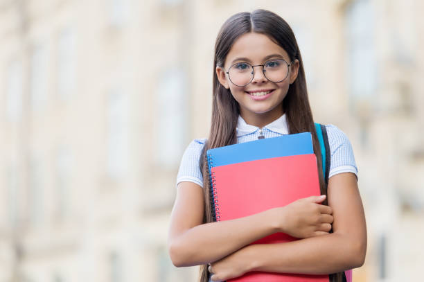 istock Happy small kid smile in eyeglasses holding school books outdoors, knowledge, copy space 1351259175