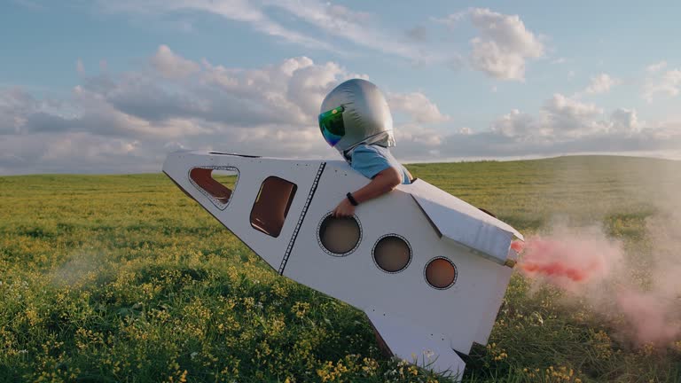 Countryside, boy plays in an astronaut helmet in nature with a cardboard model of a space shuttle, a boy runs through a field of rapeseed dreaming of flying into space, pink smoke, 4k slow motion.