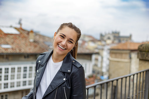 Vitoria-Gasteiz, Basque Country, Spain. September 3, 2021. Smiling young woman in white t-shirt and black leather jacket in old town