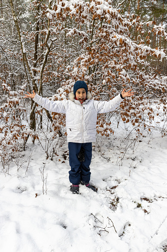 Teenager opening her arms while standing in the middle of a snow-covered forest