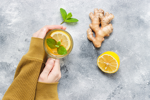 Tea with lemon, ginger root and mint leaf in hands top view. Healthy drink during autumn and winter season